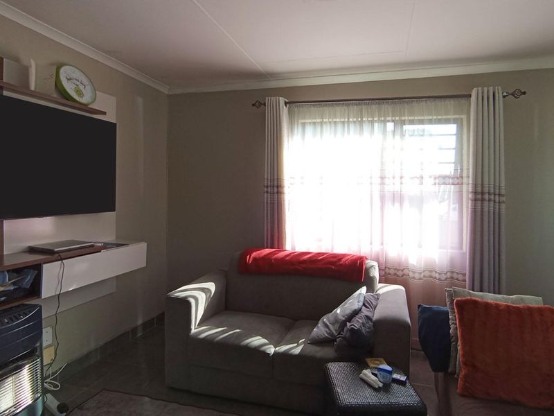 A comfortable living room featuring tiled flooring, coved ceilings, and a built-in media unit, providing a functional space for relaxation.