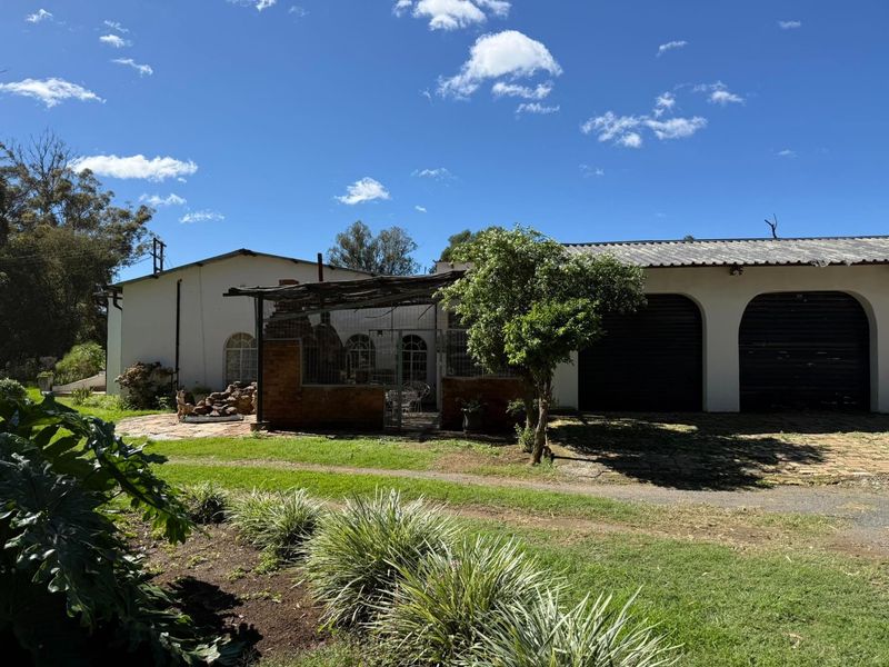 Rear view of the farm property featuring a covered brick braai area, paved courtyard, and multiple garage bays with arched entrances.