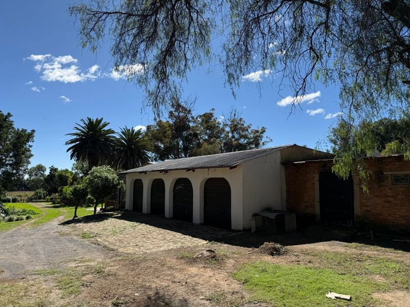 A rustic farm-style garage building featuring multiple arched bays, brick construction, and a corrugated metal roof set within a rural landscape.