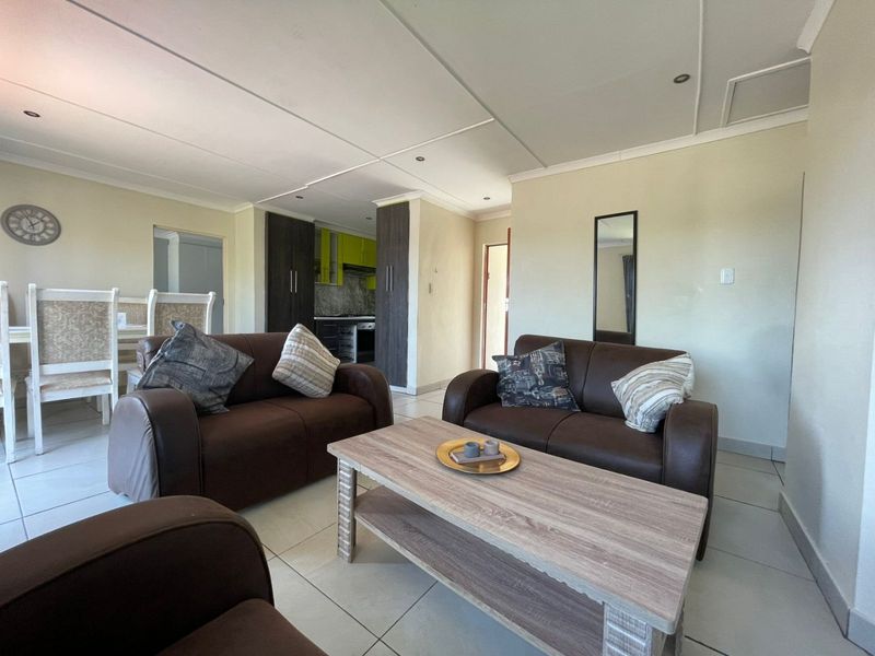Open-plan living and dining area featuring tiled flooring, recessed lighting, and a compact kitchen with built-in cabinetry and integrated appliances.