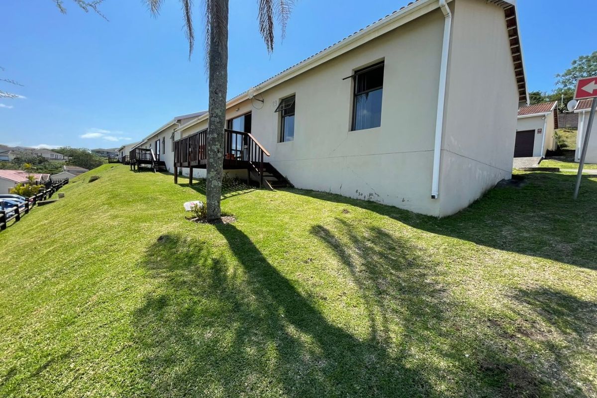 Rear view of the townhouse featuring a raised timber deck, tiled roof, and a sloping lawn area.