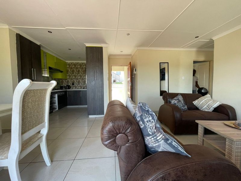 Open-plan living area featuring a modern kitchen with built-in cabinetry, oven, and extractor fan, seamlessly flowing into the lounge space with tiled flooring.