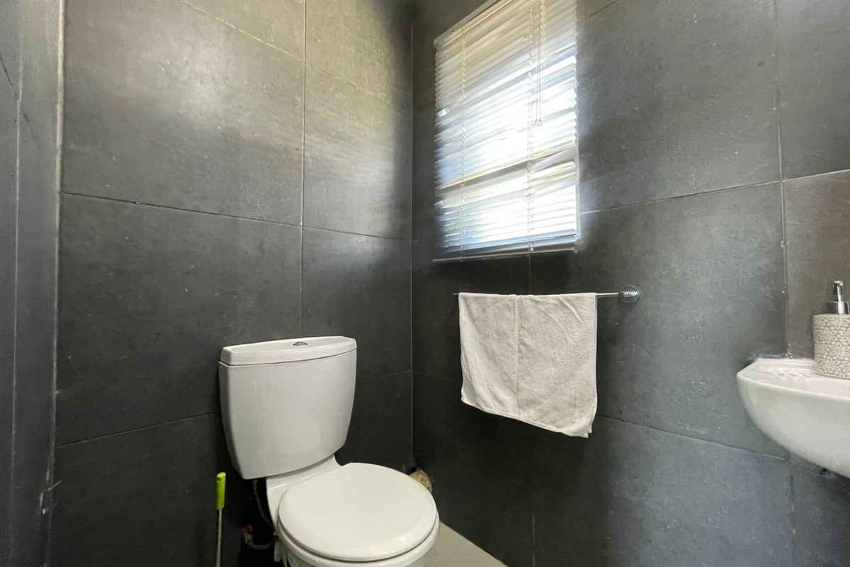 A compact guest bathroom featuring modern dark grey wall tiles, a white toilet, and a wall-mounted basin with a window for natural light.