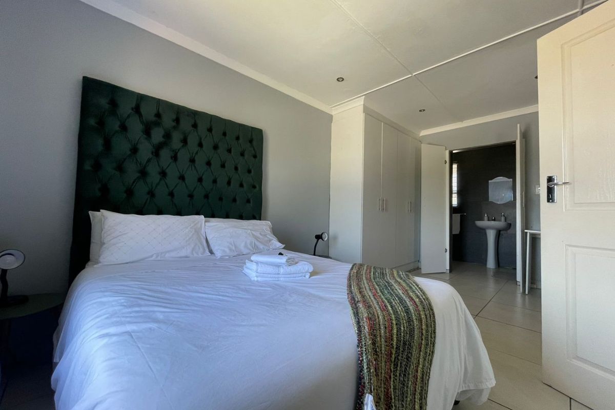 Spacious bedroom featuring built-in cupboards, tiled flooring, and an en-suite bathroom area with a pedestal basin.