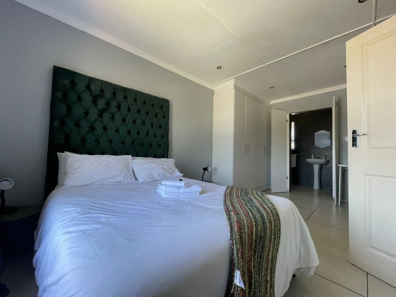 Spacious bedroom featuring built-in cupboards, tiled flooring, and an en-suite bathroom area with a pedestal basin.