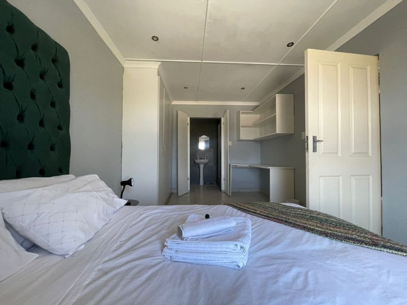 A bedroom featuring built-in cupboards, a dedicated desk area with shelving, and direct access to an en-suite bathroom.
