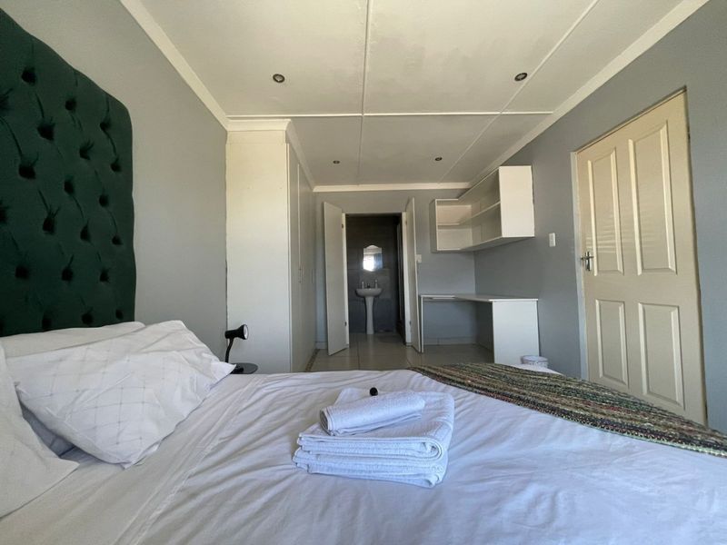 A bedroom featuring built-in cupboards, a built-in desk area, and direct access to an en-suite bathroom with a pedestal basin.