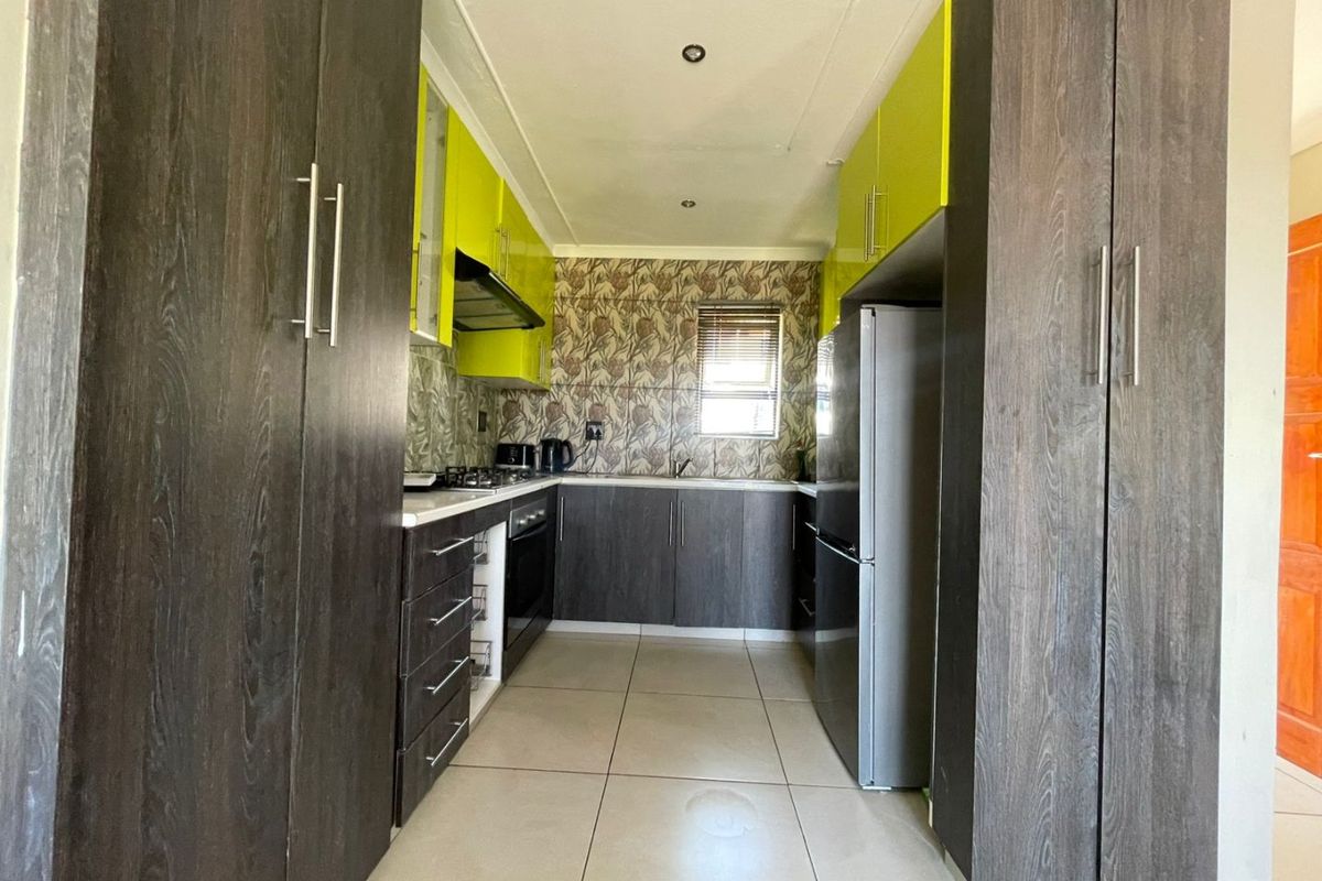 A galley-style kitchen featuring dark wood-grain and lime green cabinetry, tiled flooring, built-in oven, hob, and extractor fan.