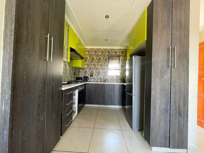A galley-style kitchen featuring dark wood-grain and lime green cabinetry, tiled flooring, built-in oven, hob, and extractor fan.