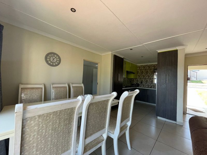 Open plan dining area flowing into a compact kitchen with built-in cabinetry and tiled flooring.