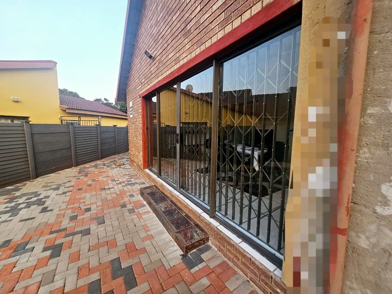 Rear exterior view featuring a brick facade, paved patio area, and sliding glass doors secured with metal security gates.
