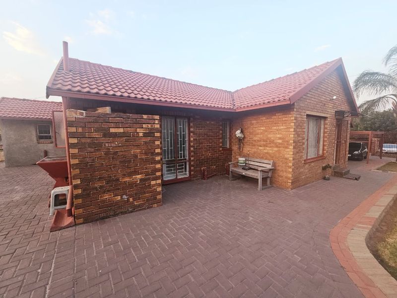 Rear exterior view of a face brick house featuring a paved patio area and tiled roof.