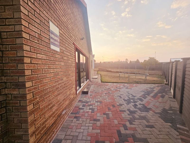 A rear exterior view featuring a paved patio area, face brick wall, and sliding glass doors leading into the home, set against a fenced garden.