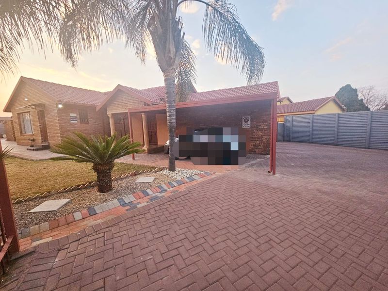 Front view of a brick house featuring a paved driveway, covered carport, and landscaped garden area.