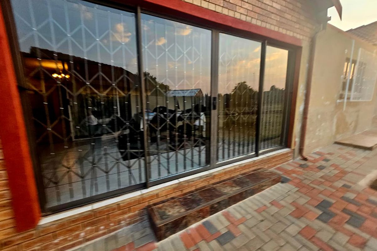 Rear exterior view of the property featuring a brick facade, large sliding glass doors with security gates, and a paved patio area.