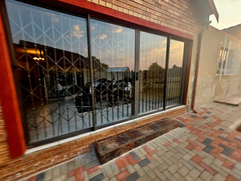 Rear exterior view of the property featuring a brick facade, large sliding glass doors with security gates, and a paved patio area.