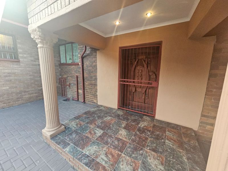 A covered front entrance porch featuring a decorative column, tiled flooring, and a secure metal gate over the main door.