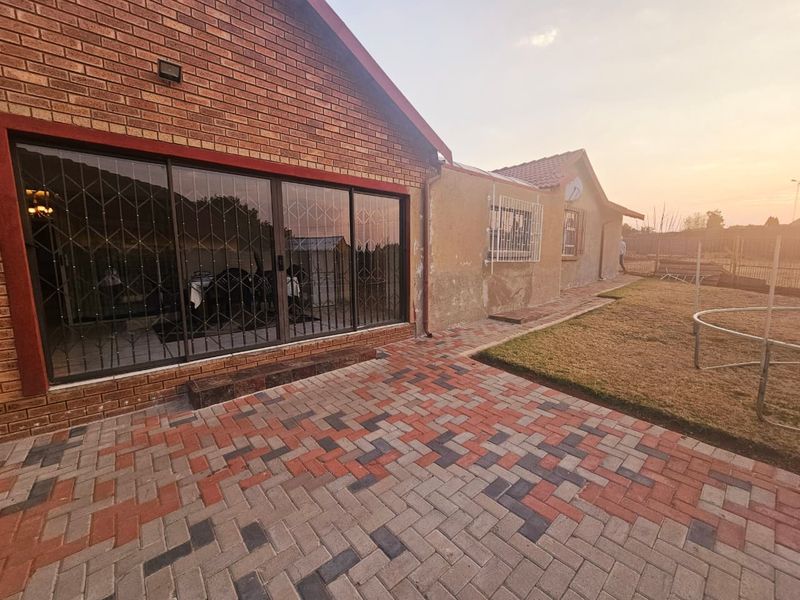 Rear view of the property featuring a paved patio area, brick facade, and sliding glass doors with security gates leading into the home.