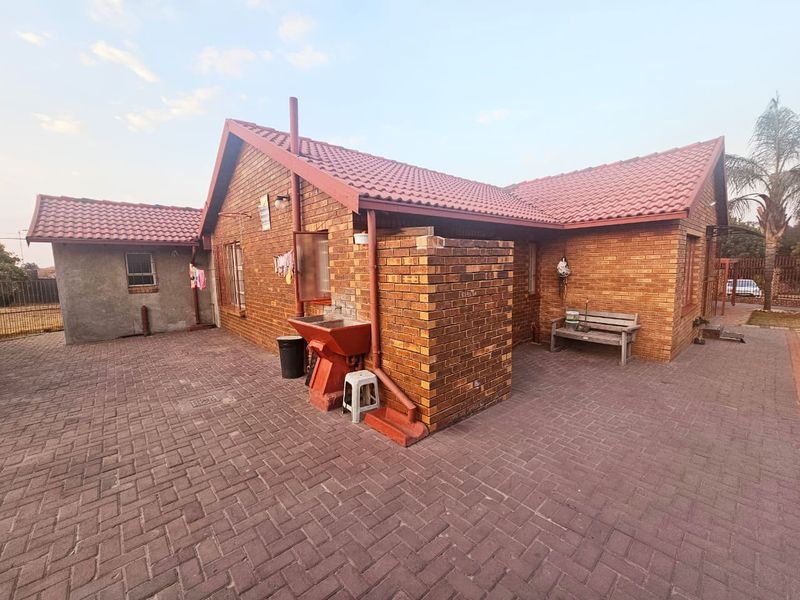 Rear view of the property featuring a face brick facade, tiled roof, and a paved courtyard area with an external wash basin.