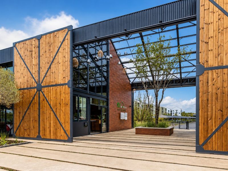 Modern architectural entrance featuring a striking combination of timber cladding, steel framing, and brickwork with a covered walkway and integrated landscaping.