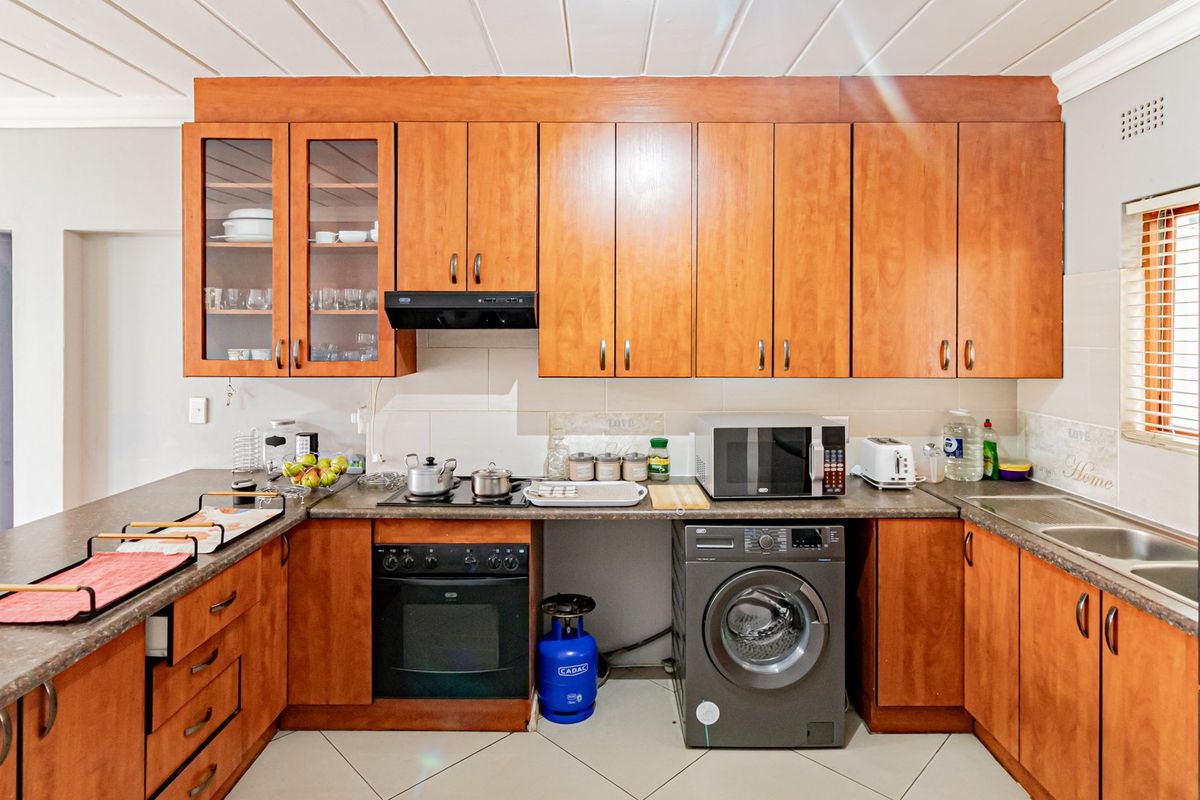 A functional kitchen featuring warm-toned wooden cabinetry, laminate countertops, built-in oven, hob, and integrated laundry appliance space.