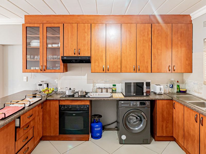 A functional kitchen featuring warm-toned wooden cabinetry, laminate countertops, built-in oven, hob, and integrated laundry appliance space.