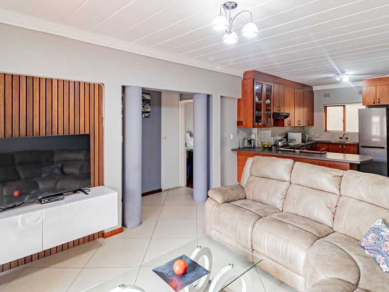 Open-plan living area featuring a wooden slat feature wall, tiled floors, and a functional kitchen with wooden cabinetry and integrated appliances.