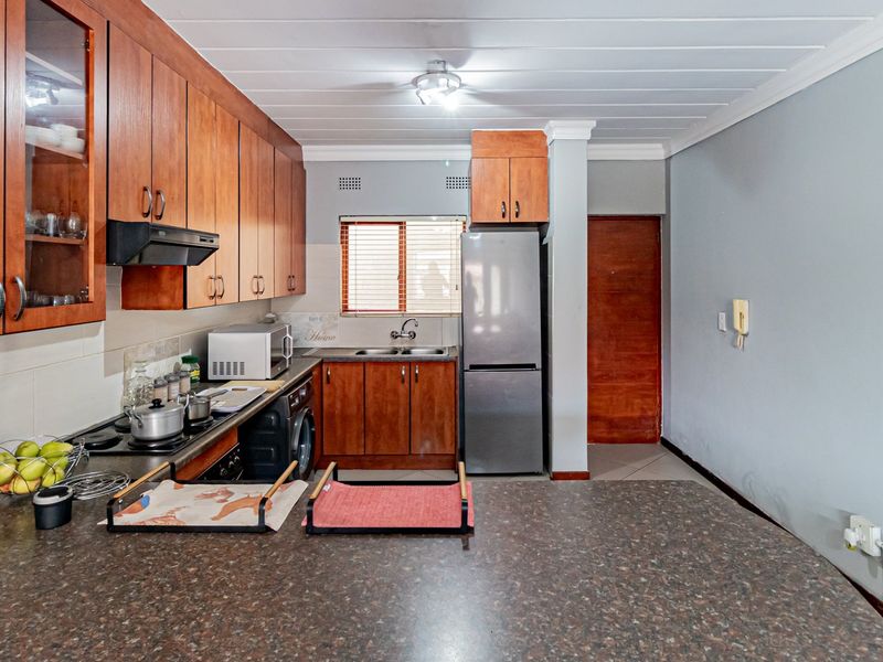 A functional kitchen featuring wooden cabinetry, laminate countertops, a built-in hob with extractor fan, and a stainless steel sink.