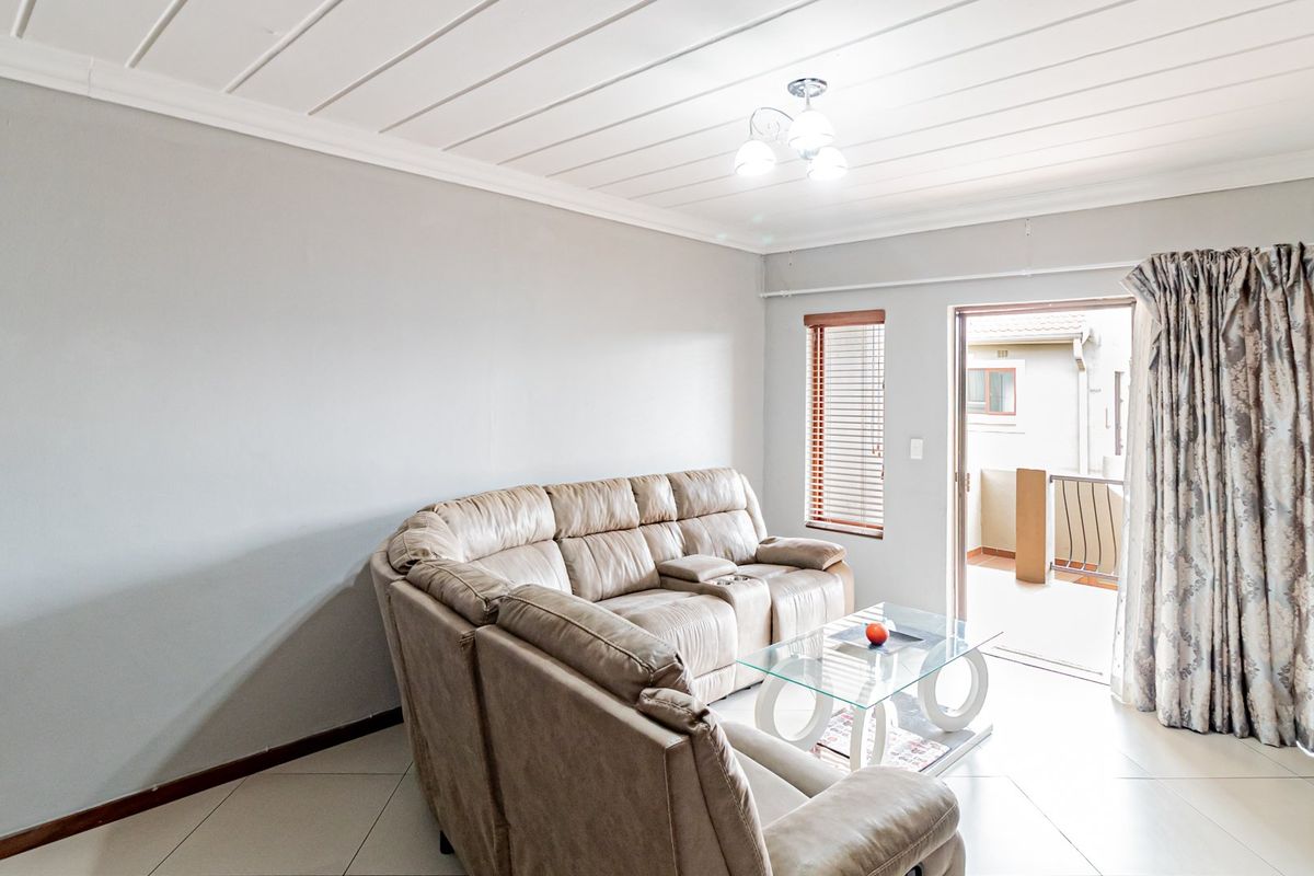 A bright living room featuring tiled flooring, a tongue and groove ceiling, and direct access to an outdoor patio area through a sliding door.