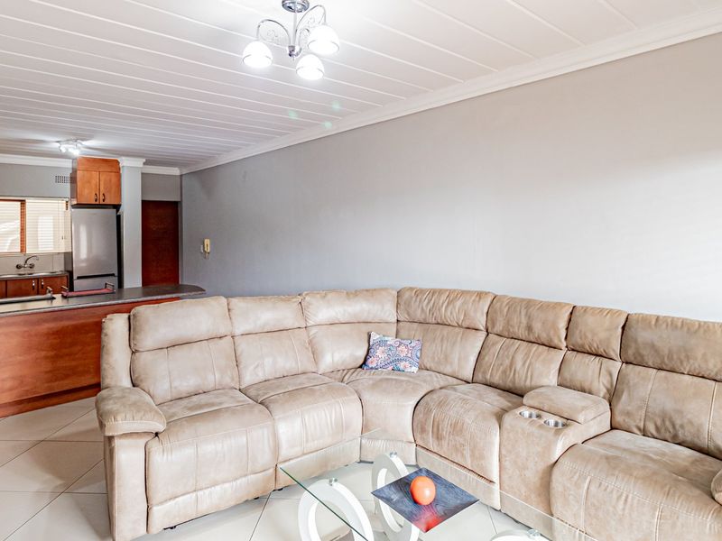 Open-plan living area featuring tiled flooring, panelled ceilings, and a functional kitchen with wooden cabinetry and a breakfast counter.