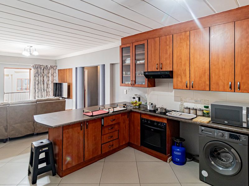 Open-plan living area featuring a kitchen with wooden cabinetry, integrated appliances, and tiled flooring, flowing into a comfortable lounge space.