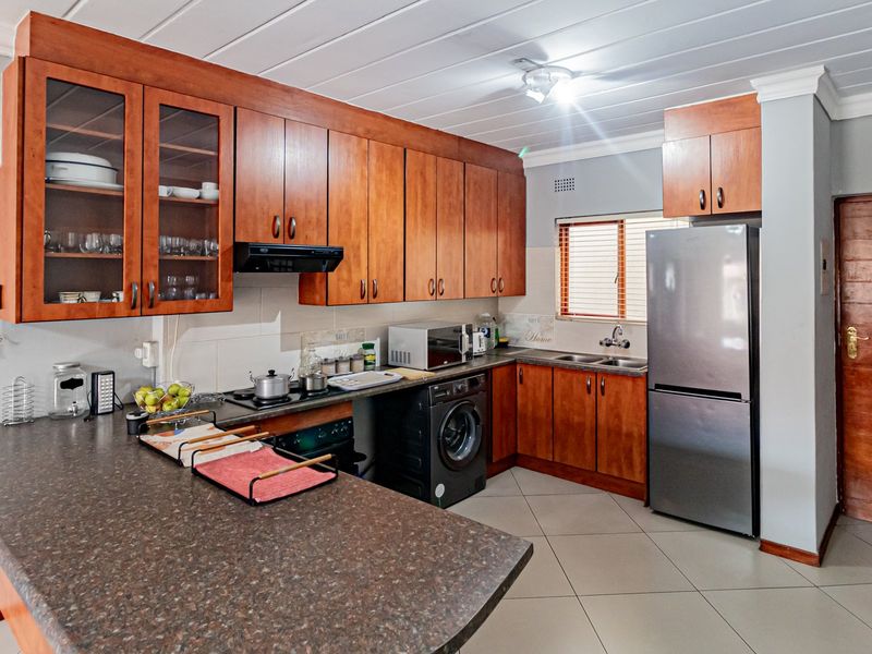A functional kitchen featuring warm-toned wooden cabinetry, laminate countertops, tiled flooring, and integrated appliances, offering a practical layout for daily meal preparation.