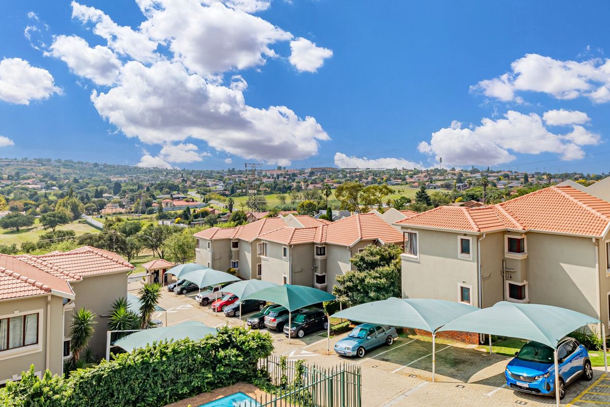 Aerial view of a townhouse complex featuring terracotta tiled roofs, covered parking bays, and a communal swimming pool set against a scenic landscape.