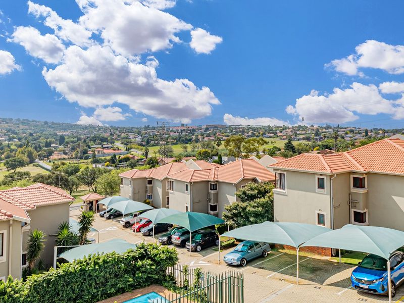 Aerial view of a townhouse complex featuring terracotta tiled roofs, covered parking bays, and a communal swimming pool set against a scenic landscape.