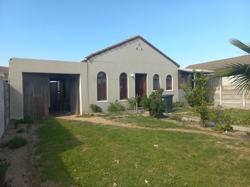 Front view of a single-story house featuring a tiled roof, arched windows, and an attached garage with a weathered timber door.