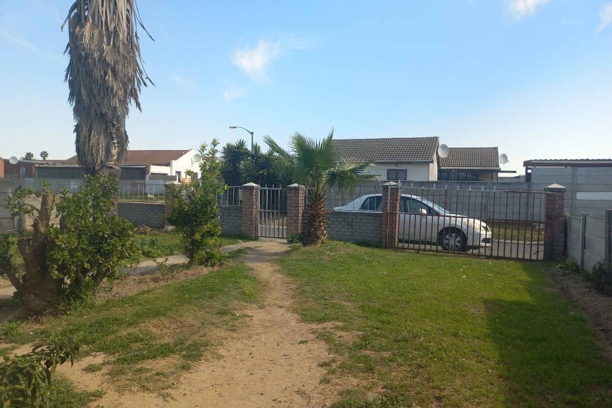 A rear garden area featuring a lawn, brick boundary walls, and metal access gates.