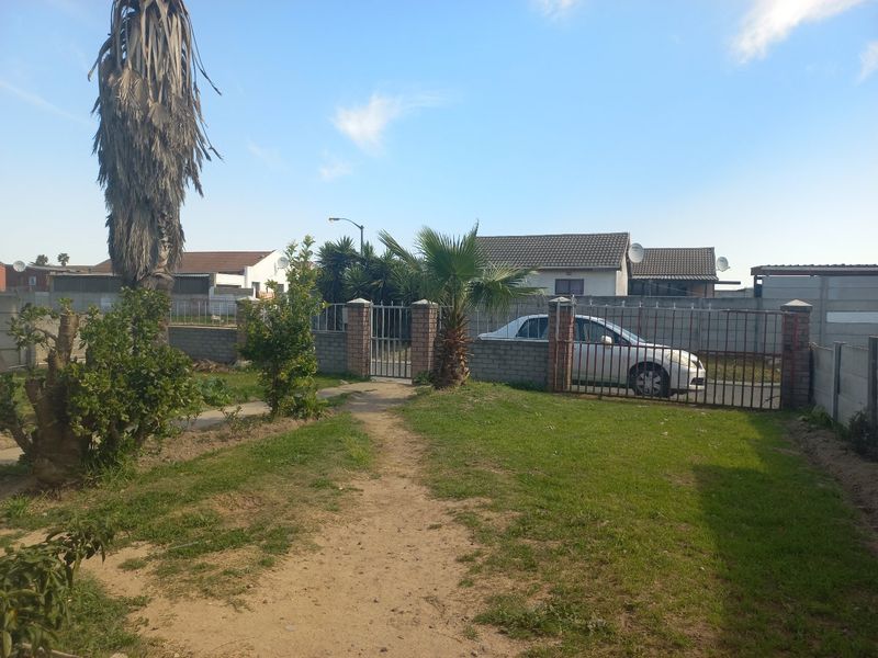 A rear garden area featuring a lawn, brick boundary walls, and metal access gates.
