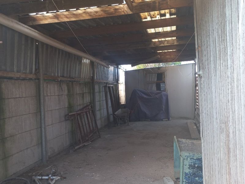 A covered outdoor utility or storage area featuring a corrugated iron roof with translucent panels and precast concrete walling.