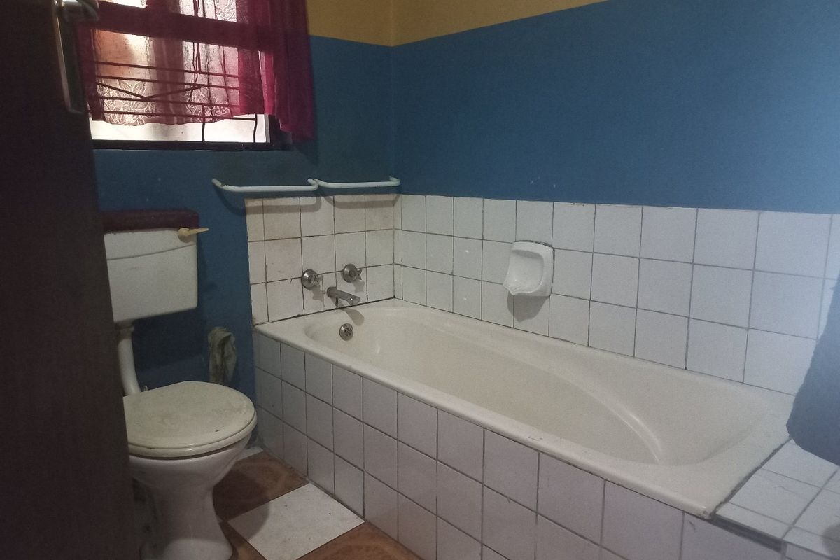 A functional bathroom featuring a standard bathtub, toilet, and tiled finishes, offering a blank canvas for potential modernization and cosmetic updates.