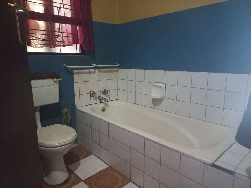 A functional bathroom featuring a standard bathtub, toilet, and tiled finishes, offering a blank canvas for potential modernization and cosmetic updates.