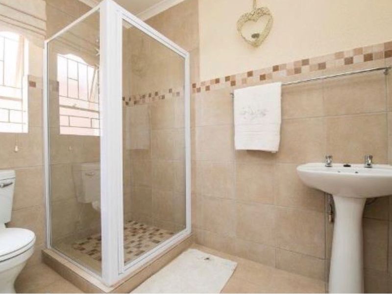 A functional bathroom featuring a glass shower enclosure, pedestal basin, and toilet with neutral wall and floor tiling.