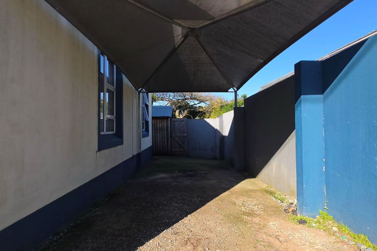 A side exterior area featuring a shade sail covering a paved driveway, enclosed by boundary walls.