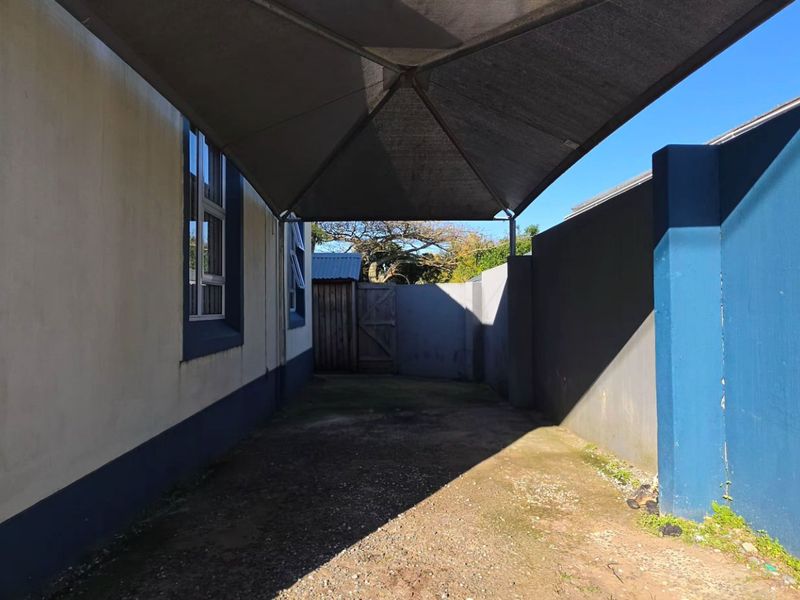 A side exterior area featuring a shade sail covering a paved driveway, enclosed by boundary walls.