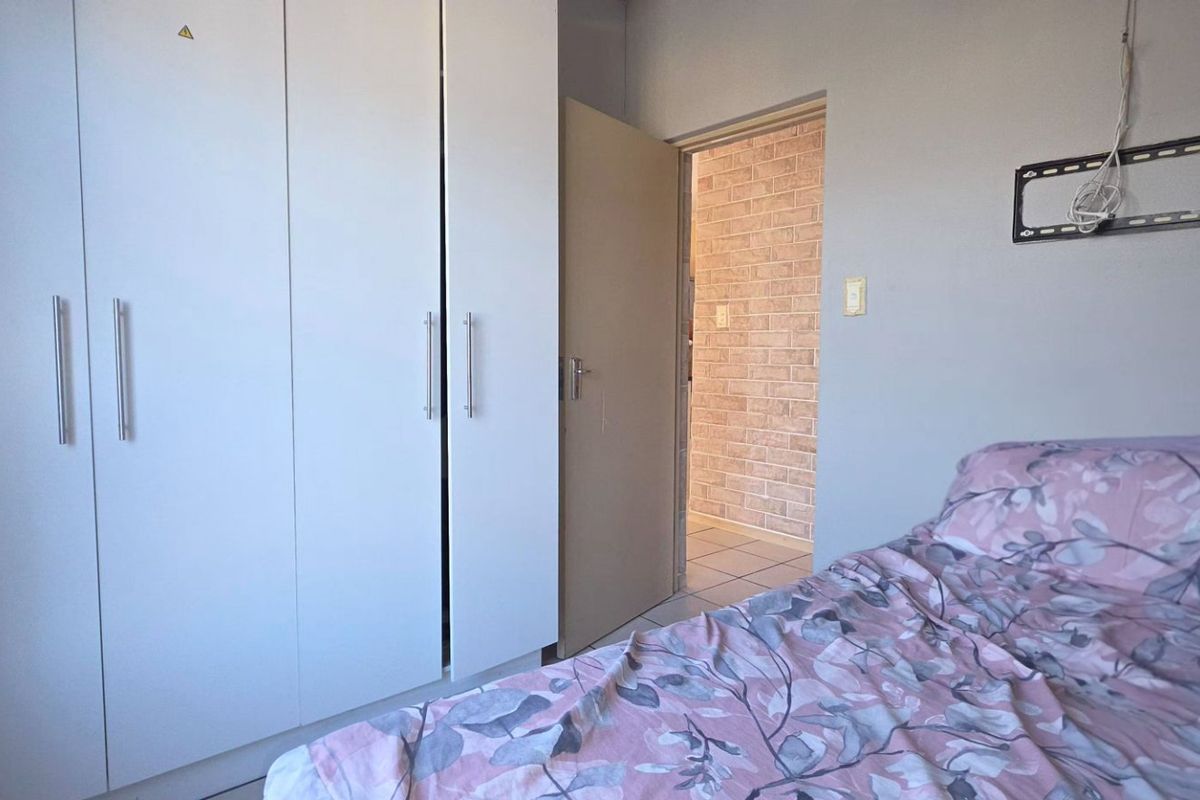 A bedroom featuring built-in cupboards and tiled flooring, with a doorway leading to an adjacent space with exposed brick wall finishes.