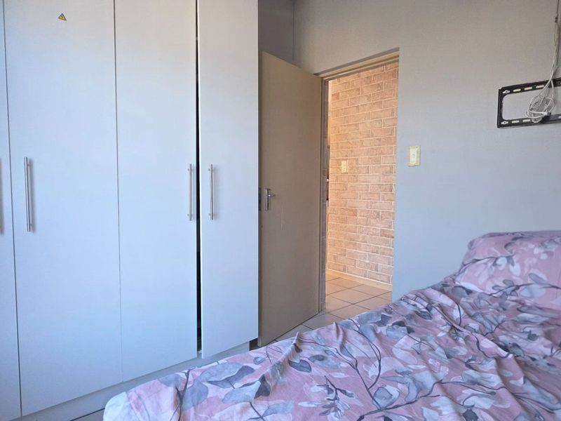 A bedroom featuring built-in cupboards and tiled flooring, with a doorway leading to an adjacent space with exposed brick wall finishes.