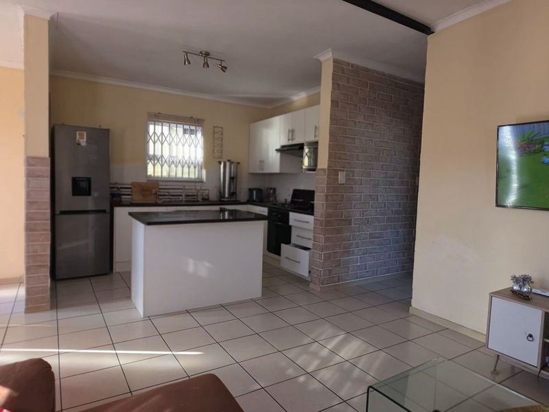 Open-plan living area featuring a kitchen with a central island, tiled flooring, and a brick feature wall, creating a functional and connected living space.