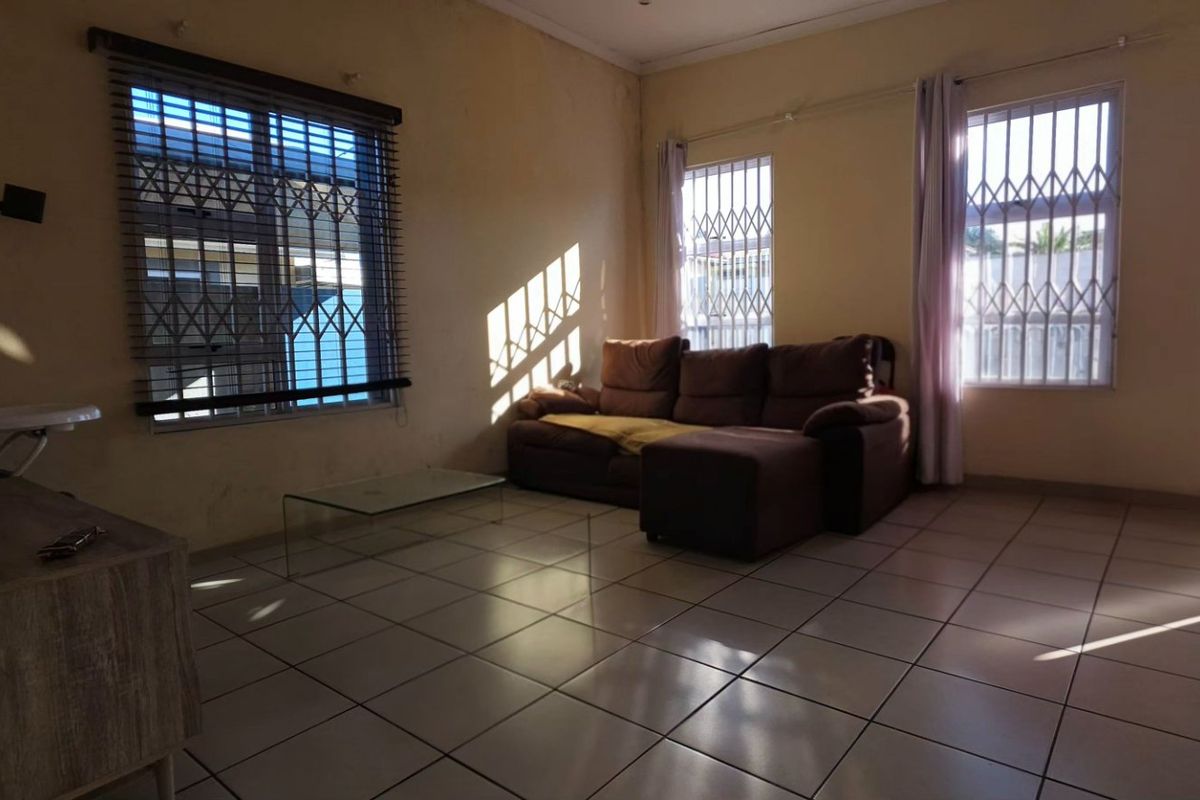 A living room featuring tiled flooring and windows fitted with security bars and blinds, requiring cosmetic updates to improve the overall aesthetic.