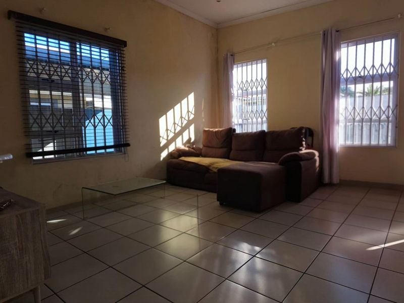 A living room featuring tiled flooring and windows fitted with security bars and blinds, requiring cosmetic updates to improve the overall aesthetic.