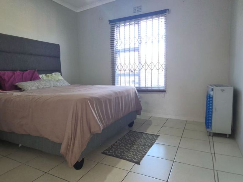 A functional bedroom featuring tiled flooring, security bars on the window, and venetian blinds.