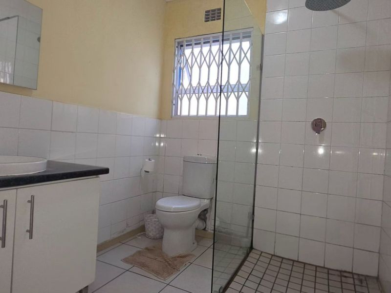 A functional bathroom featuring a vanity with basin, a toilet, and a walk-in shower with a glass screen and tiled finishes.
